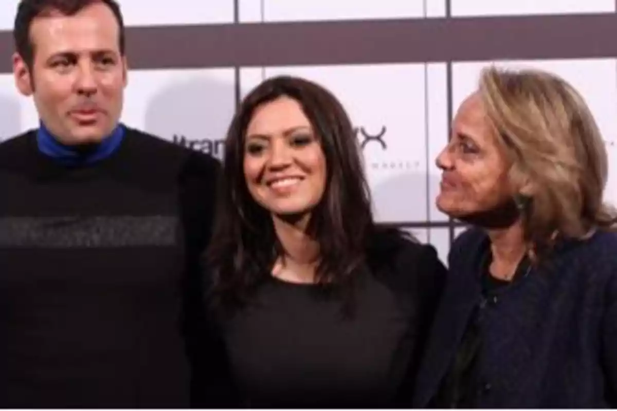 Tres personas posan sonrientes frente a un fondo con cuadros blancos y grises Tres personas posan sonrientes frente a un fondo con cuadros blancos y grises