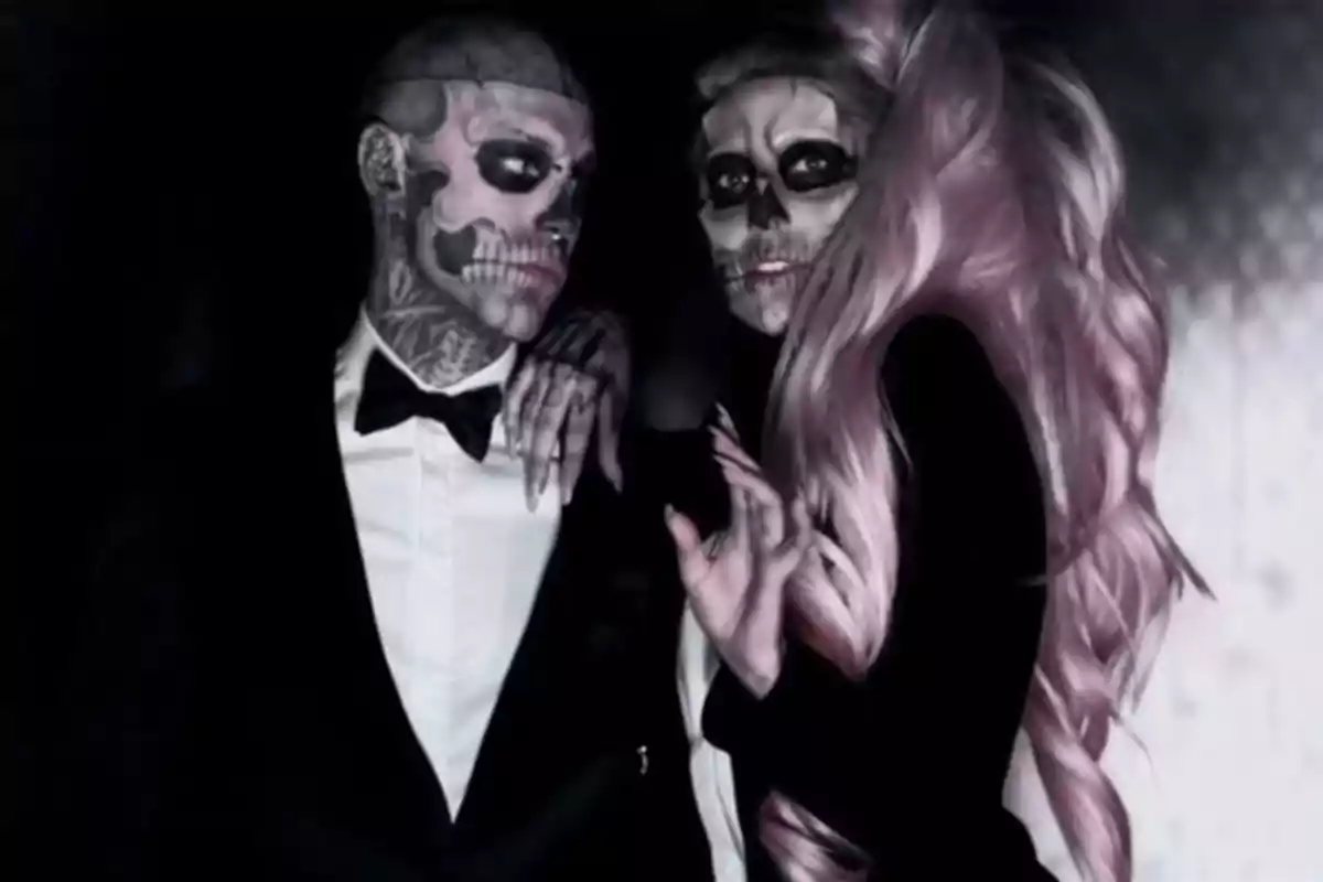 Dos personas vestidas de manera elegante con maquillaje de calavera en el rostro posan juntas en un ambiente oscuro Dos personas vestidas de manera elegante con maquillaje de calavera en el rostro posan juntas en un ambiente oscuro