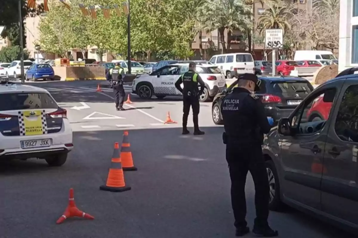 Control policial en una calle con varios agentes revisando vehículos y conos naranjas delimitando el área Control policial en una calle con varios agentes revisando vehículos y conos naranjas delimitando el área