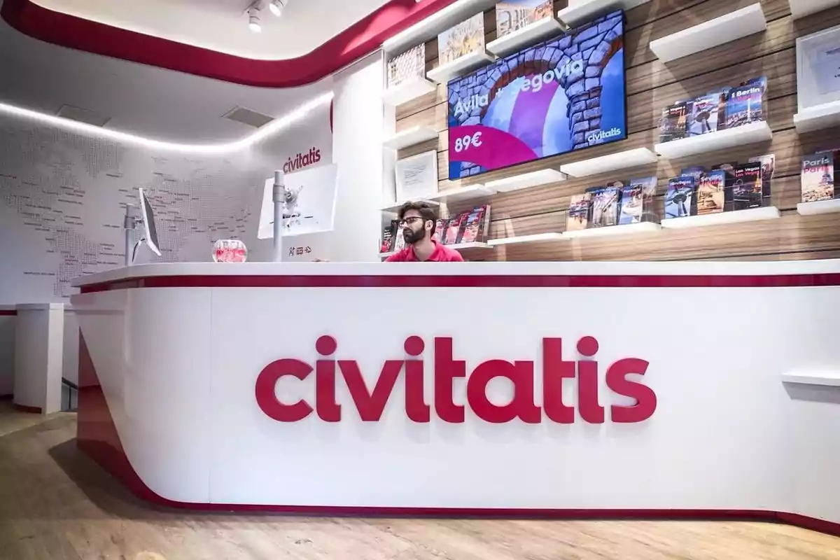 Recepción moderna de una agencia de viajes Civitatis con un mostrador blanco y rojo, un empleado atendiendo y folletos turísticos en estanterías al fondo Recepción moderna de una agencia de viajes Civitatis con un mostrador blanco y rojo, un empleado atendiendo y folletos turísticos en estanterías al fondo