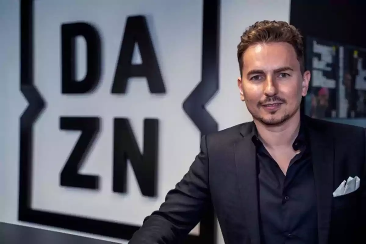 Hombre con saco oscuro posando frente a un letrero de DAZN Hombre con saco oscuro posando frente a un letrero de DAZN