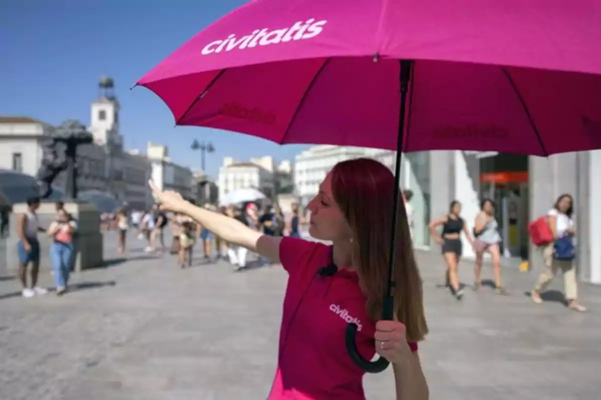 Guía turística con paraguas rosa de Civitatis señalando una dirección en una plaza concurrida Guía turística con paraguas rosa de Civitatis señalando una dirección en una plaza concurrida