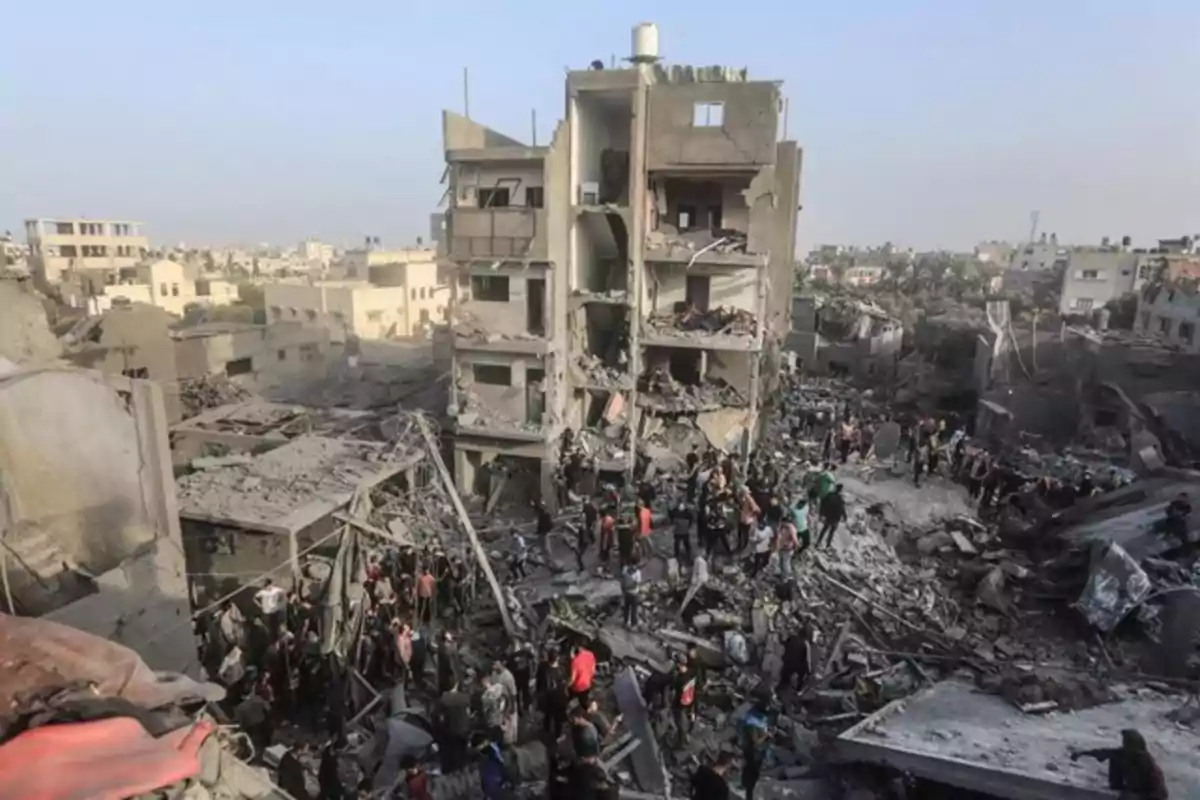 Edificio parcialmente destruido rodeado de escombros y personas entre los restos en una zona urbana afectada por un conflicto Edificio parcialmente destruido rodeado de escombros y personas entre los restos en una zona urbana afectada por un conflicto