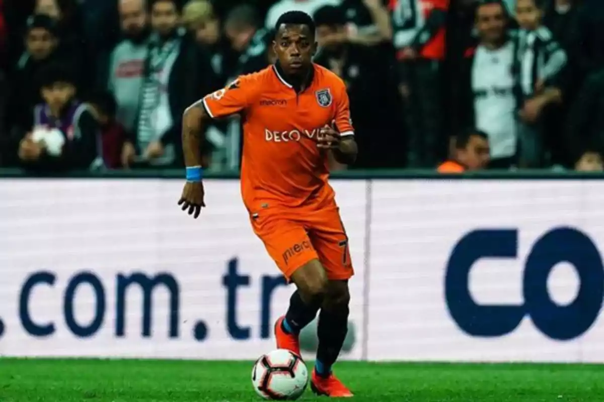 Futbolista con uniforme naranja controla el balón durante un partido en un estadio lleno de espectadores Futbolista con uniforme naranja controla el balón durante un partido en un estadio lleno de espectadores