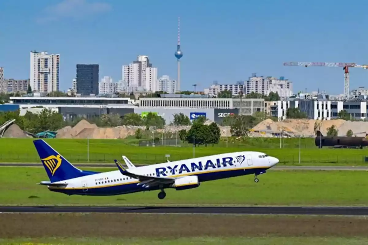 Avión de Ryanair despegando en un aeropuerto con una ciudad y una torre de telecomunicaciones al fondo Avión de Ryanair despegando en un aeropuerto con una ciudad y una torre de telecomunicaciones al fondo