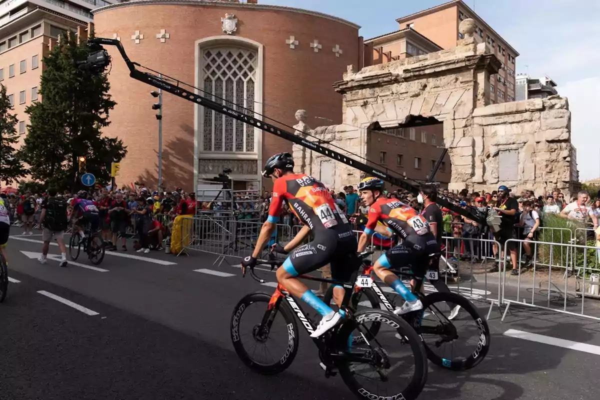 Ciclistas profesionales compitiendo en una carrera urbana con público y estructuras históricas de fondo Ciclistas profesionales compitiendo en una carrera urbana con público y estructuras históricas de fondo