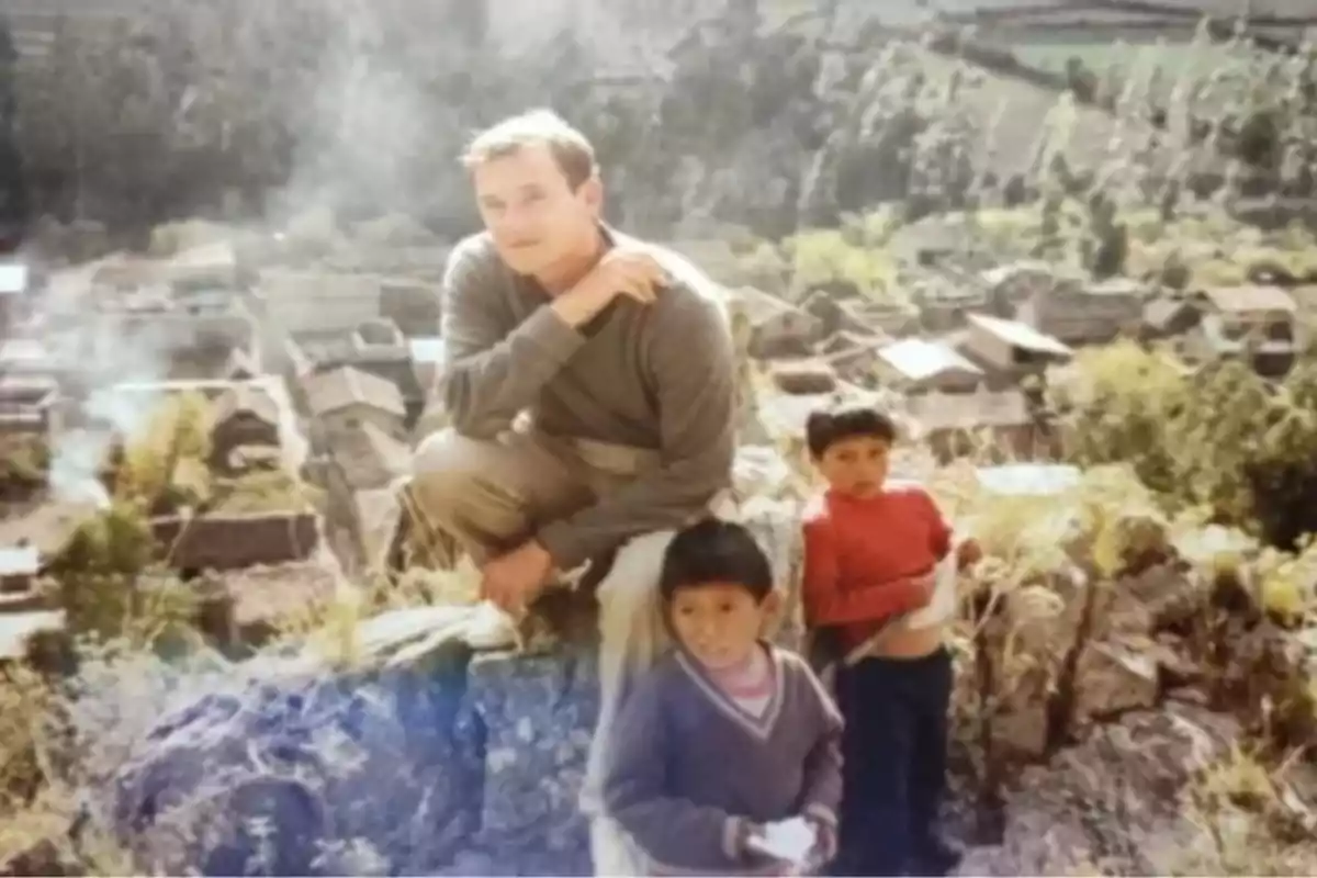 Un hombre y dos niños posan en una colina con un pueblo y vegetación al fondo Un hombre y dos niños posan en una colina con un pueblo y vegetación al fondo