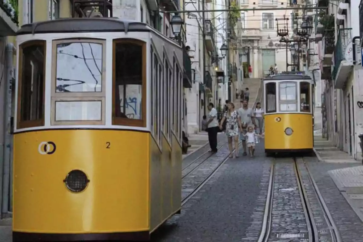 Tranvías amarillos circulando por una calle empinada con personas caminando entre los rieles en una ciudad europea