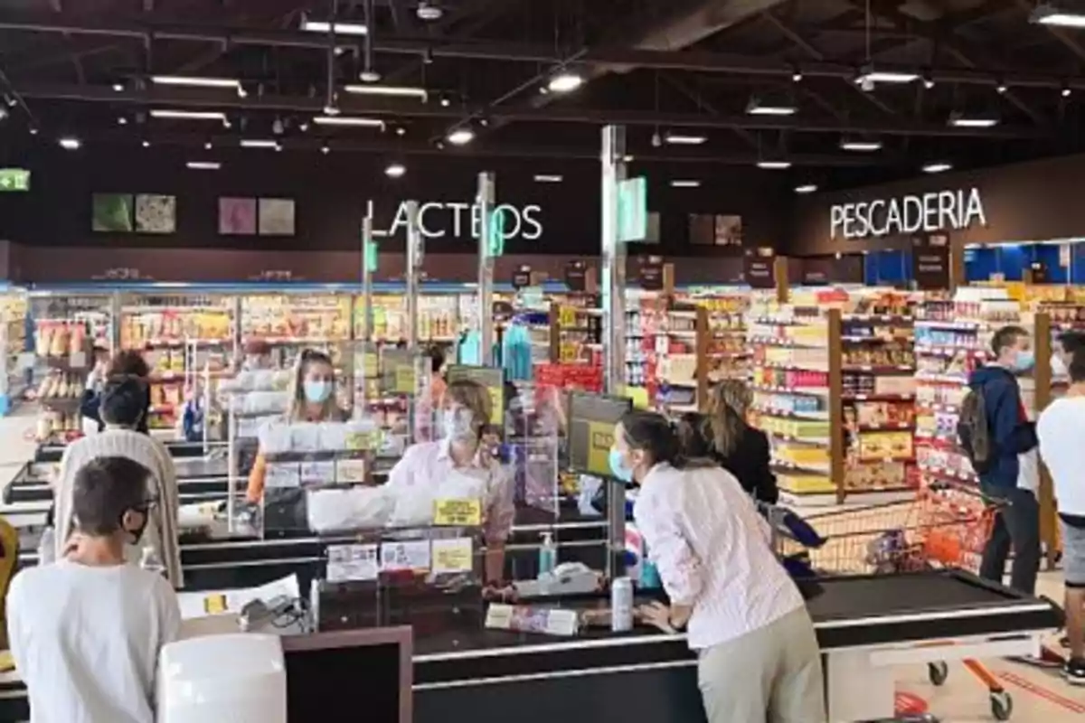 Personas haciendo fila en la caja de un supermercado usando cubrebocas mientras compran productos en diferentes secciones Personas haciendo fila en la caja de un supermercado usando cubrebocas mientras compran productos en diferentes secciones