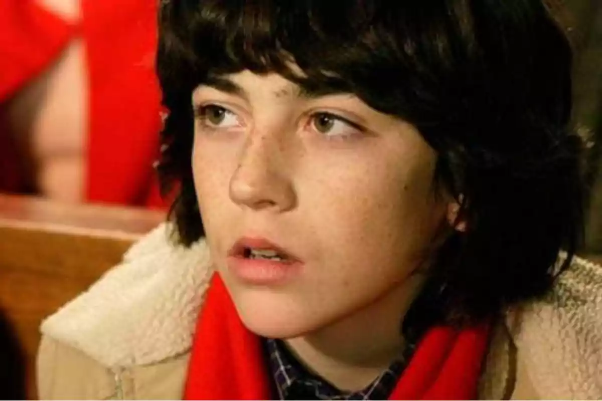 Joven de cabello oscuro y corto con expresión pensativa, usando una bufanda roja y una chaqueta beige Joven de cabello oscuro y corto con expresión pensativa, usando una bufanda roja y una chaqueta beige