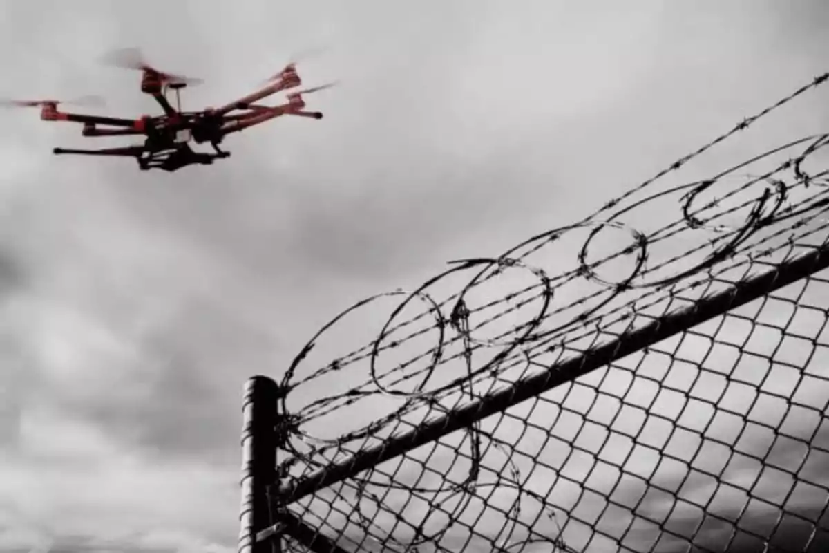 Un dron vuela cerca de una cerca de alambre con púas bajo un cielo nublado