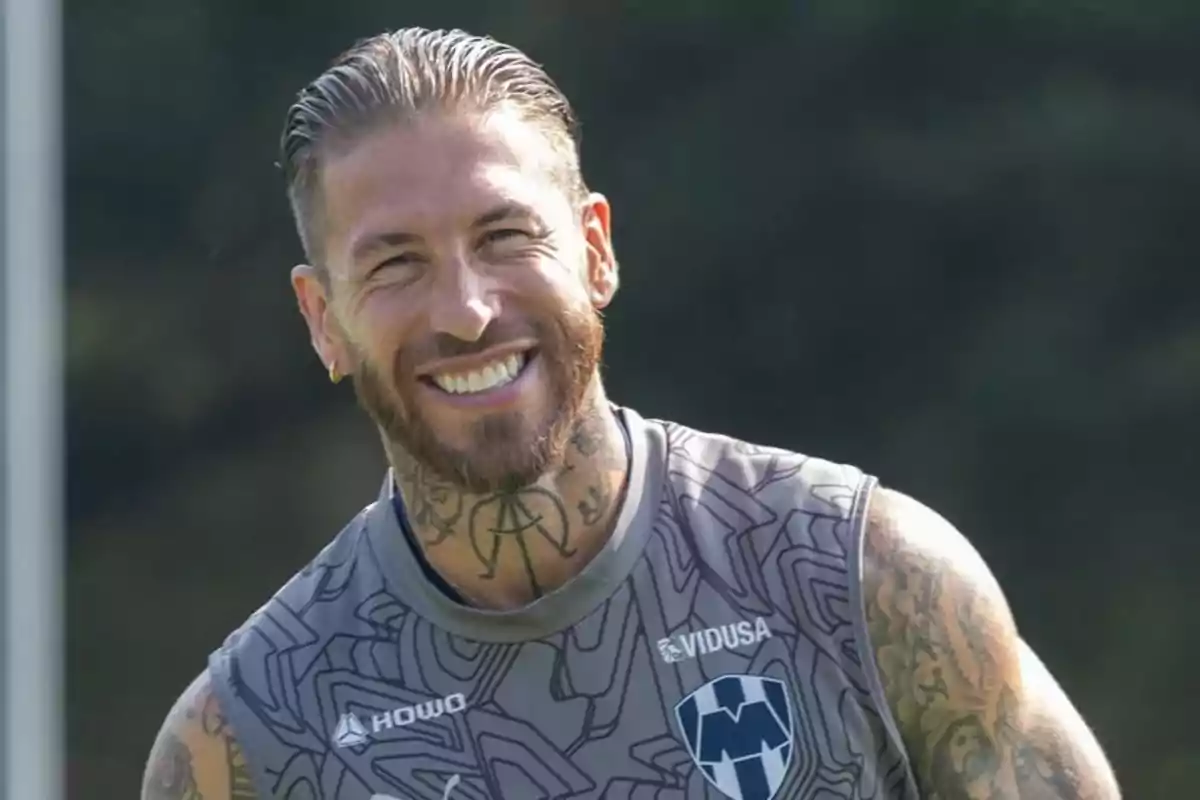 Hombre sonriente con tatuajes en el cuello y brazos usando una camiseta deportiva gris del equipo Monterrey Hombre sonriente con tatuajes en el cuello y brazos usando una camiseta deportiva gris del equipo Monterrey