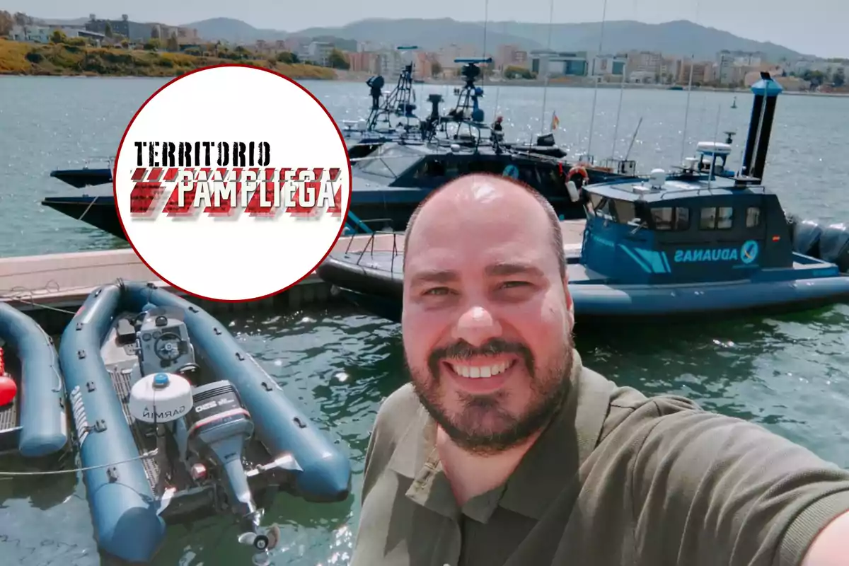 Hombre sonriente tomándose una selfie en un puerto con varias lanchas de la aduana y un logo circular de Territorio Pampliega en la esquina superior izquierda