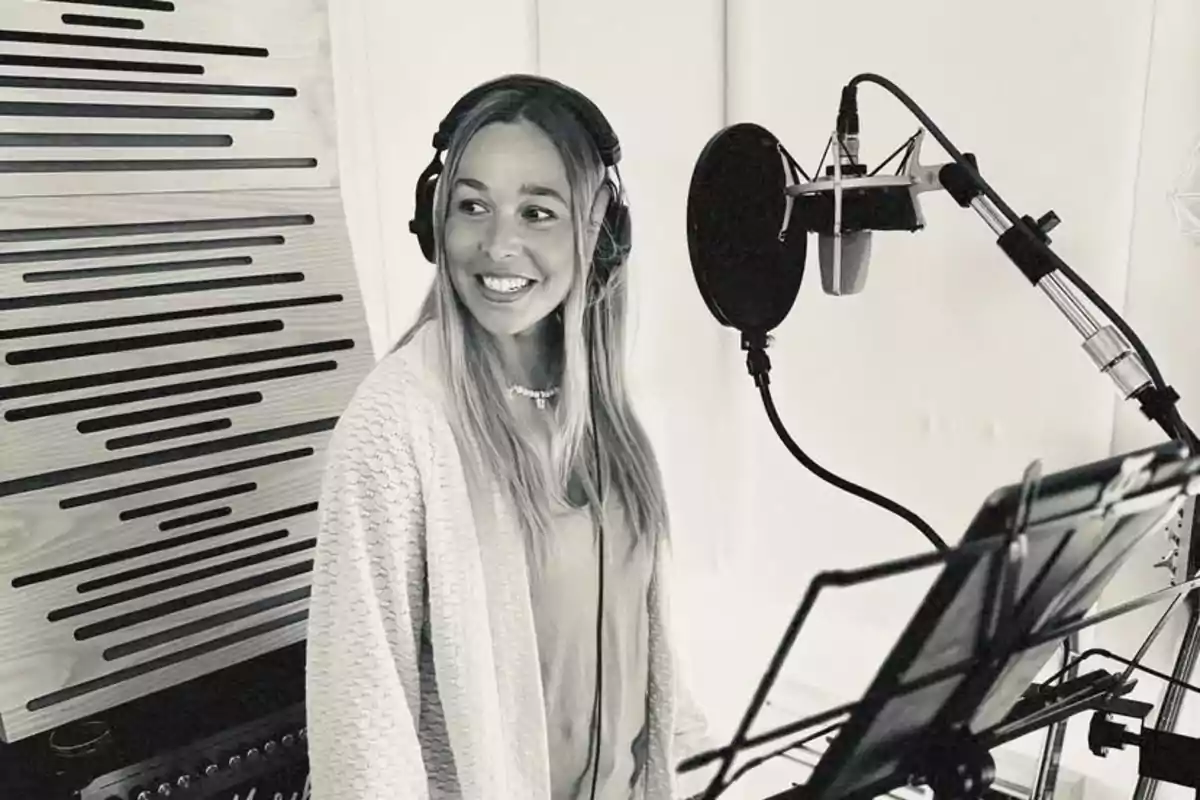 Mujer sonriente con auriculares en un estudio de grabación frente a un micrófono profesional