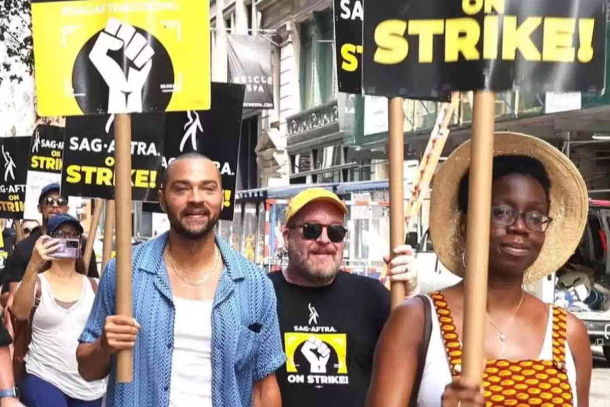 Varias personas marchan por la calle sosteniendo carteles de huelga de SAG-AFTRA con mensajes de protesta y un puño en alto Varias personas marchan por la calle sosteniendo carteles de huelga de SAG-AFTRA con mensajes de protesta y un puño en alto