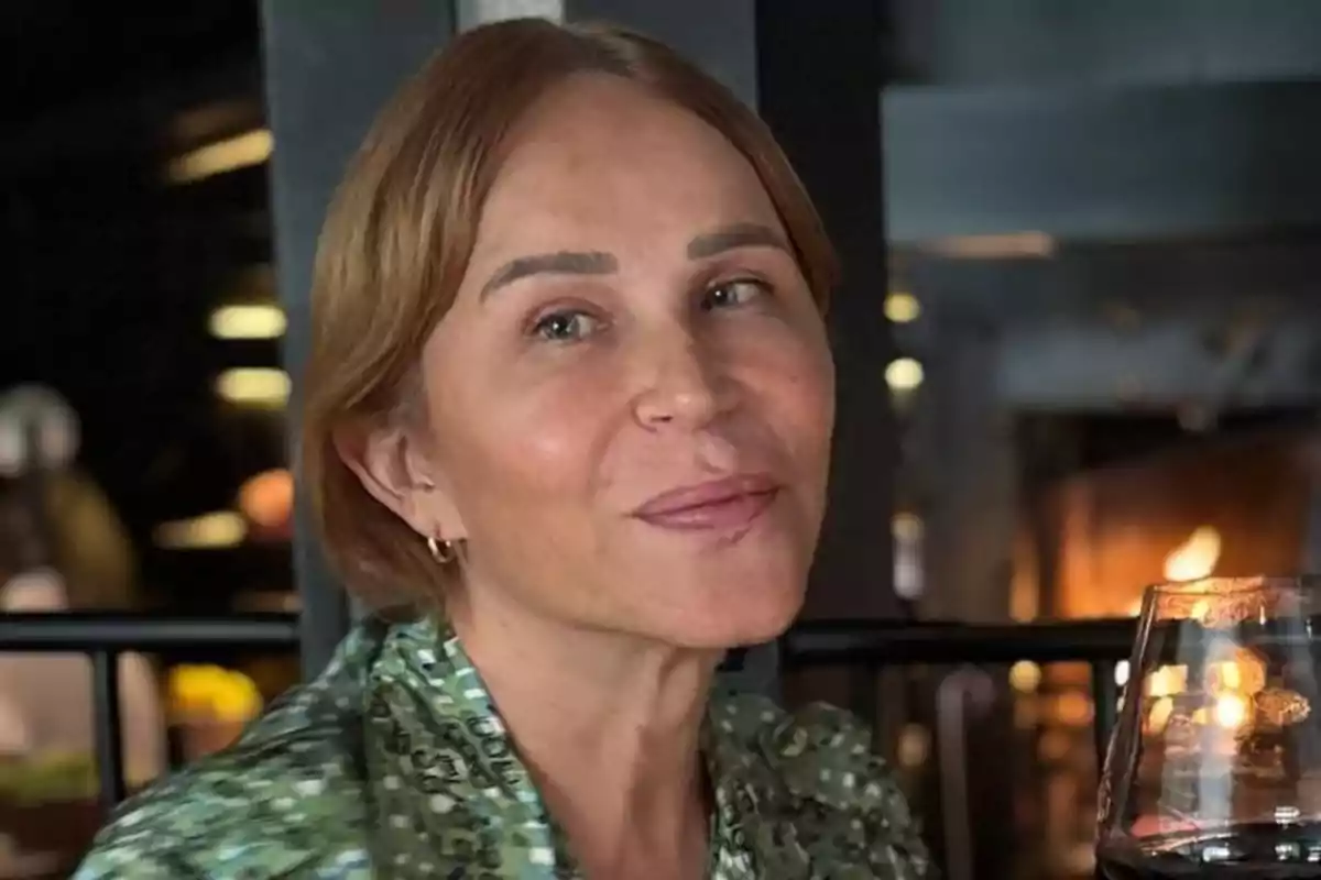 Mujer de cabello corto y rubio sonriendo mientras sostiene una copa de vino tinto en un ambiente interior elegante Mujer de cabello corto y rubio sonriendo mientras sostiene una copa de vino tinto en un ambiente interior elegante