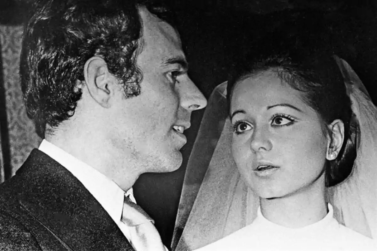 Pareja vestida de traje y vestido de novia en una fotografía en blanco y negro mirando hacia el frente Pareja vestida de traje y vestido de novia en una fotografía en blanco y negro mirando hacia el frente