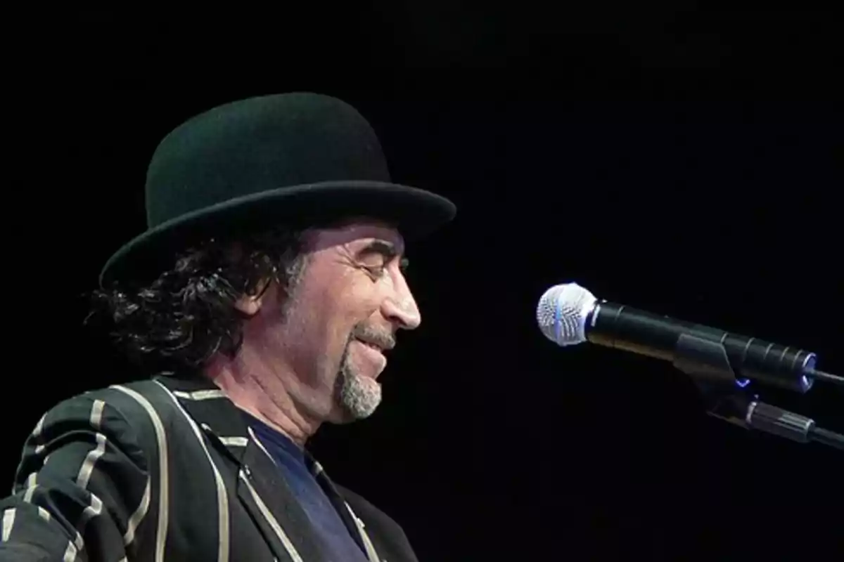 Hombre con sombrero negro y chaqueta de rayas frente a un micrófono en un escenario Hombre con sombrero negro y chaqueta de rayas frente a un micrófono en un escenario