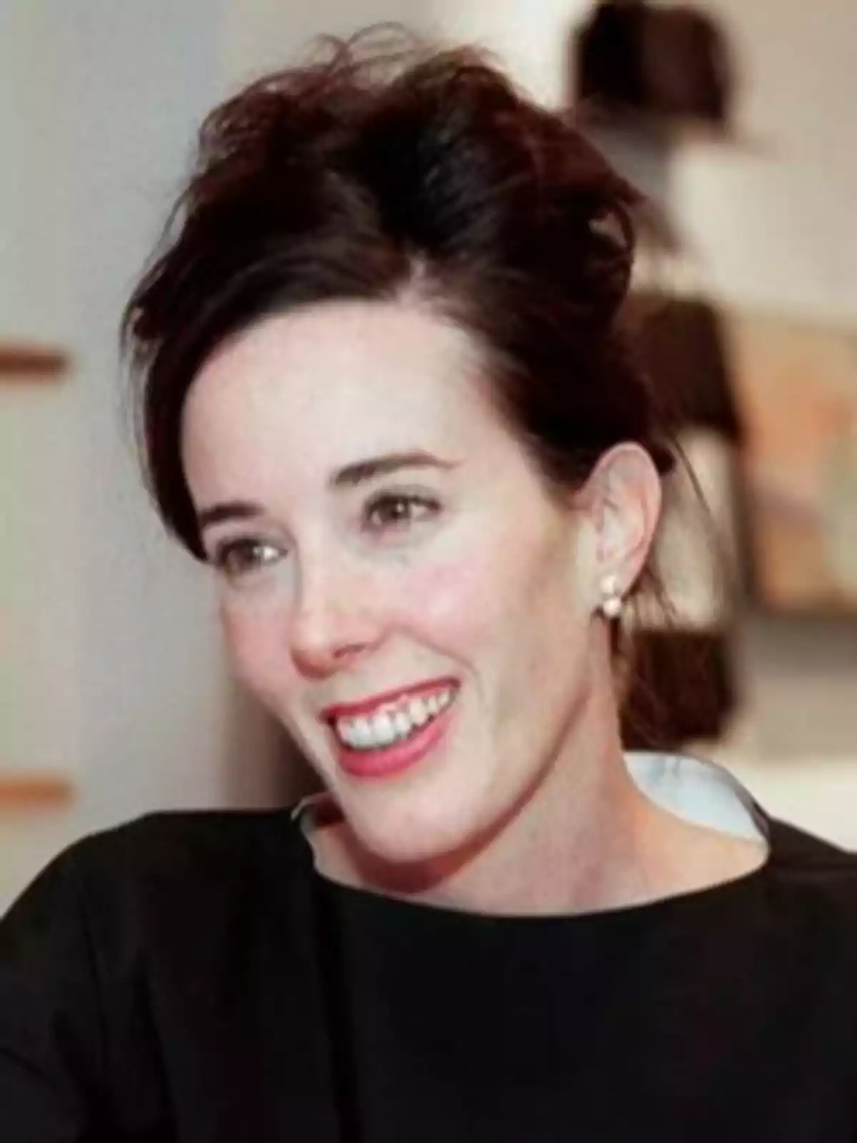 Mujer de cabello oscuro recogido, con pendientes de perla y sonrisa, usando una blusa negra Mujer de cabello oscuro recogido, con pendientes de perla y sonrisa, usando una blusa negra
