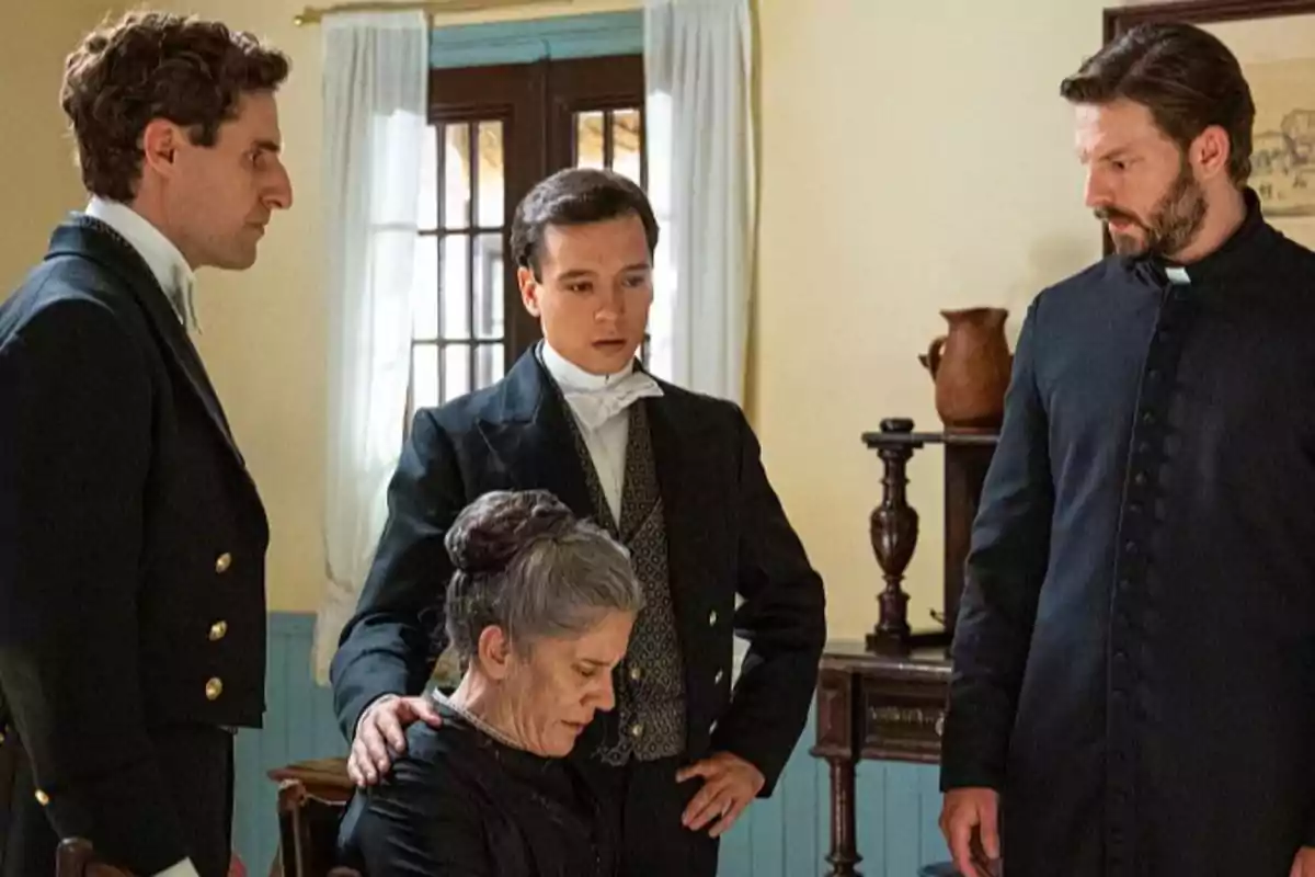Lope, Curro, Samuel y Petra con vestimenta de época están en una habitación, tres hombres de pie rodean a una mujer sentada que parece estar triste o preocupada. Captura de 'La Promesa' Lope, Curro, Samuel y Petra con vestimenta de época están en una habitación, tres hombres de pie rodean a una mujer sentada que parece estar triste o preocupada. Captura de 'La Promesa'