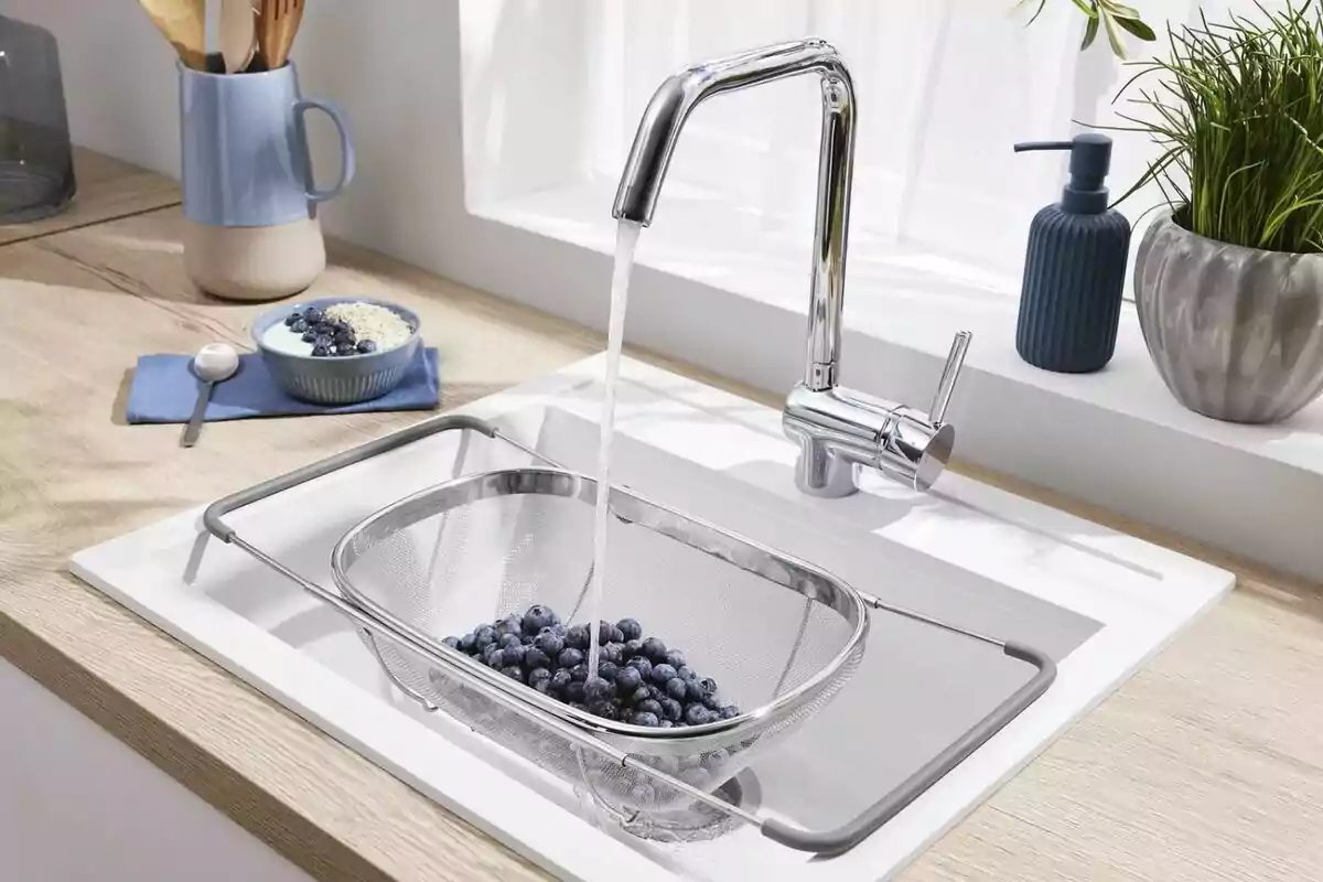 Un colador con arándanos bajo el grifo de una cocina moderna mientras se lavan las frutas Un colador con arándanos bajo el grifo de una cocina moderna mientras se lavan las frutas