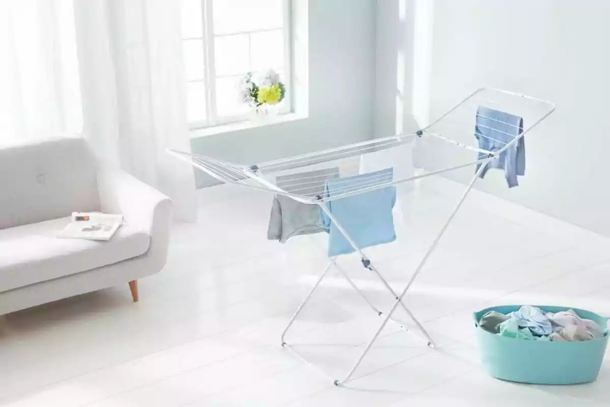 Tendedero con ropa secándose en una sala luminosa junto a una canasta de ropa y un sofá claro Tendedero con ropa secándose en una sala luminosa junto a una canasta de ropa y un sofá claro