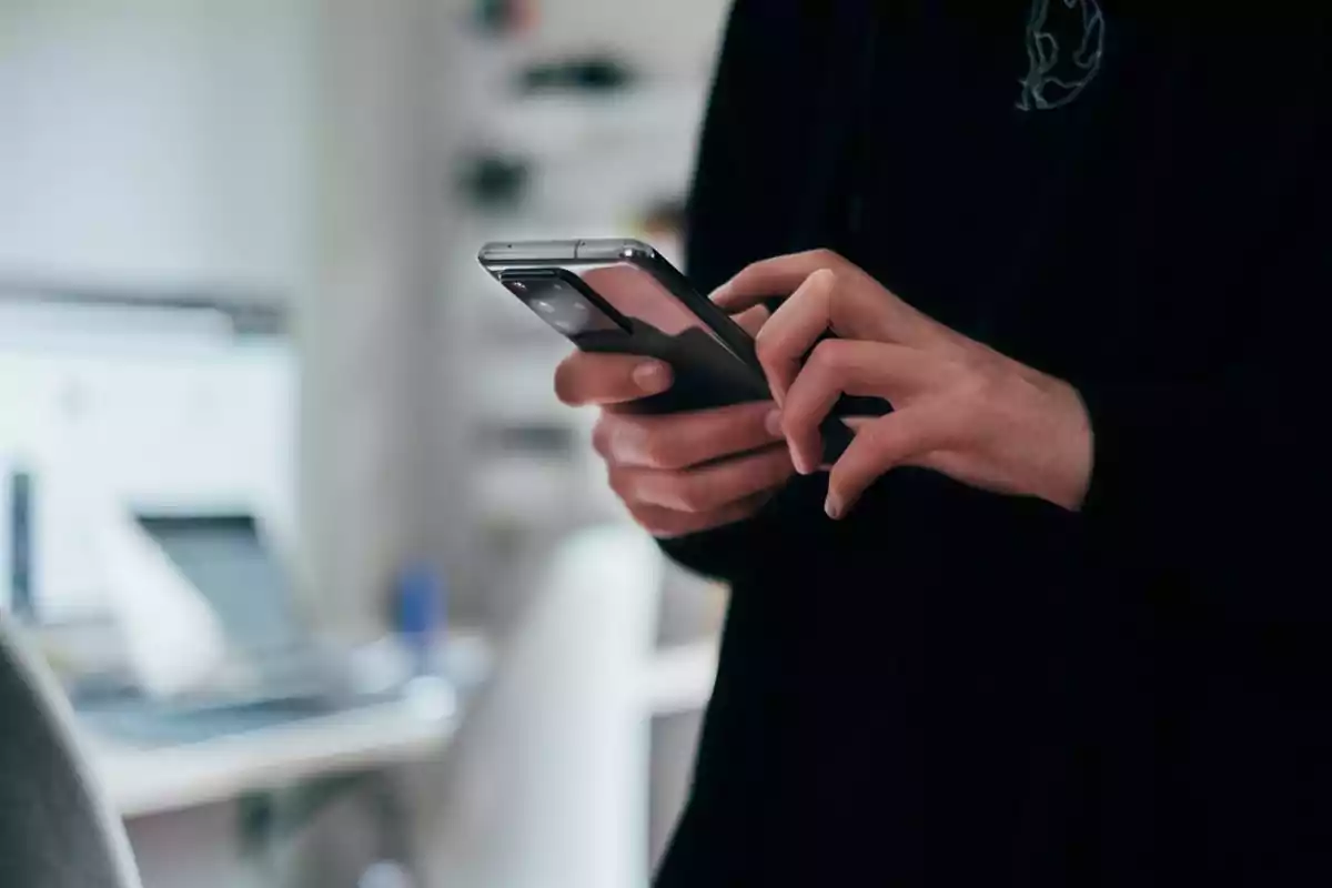 Persona usando un teléfono móvil en un entorno de oficina desenfocado