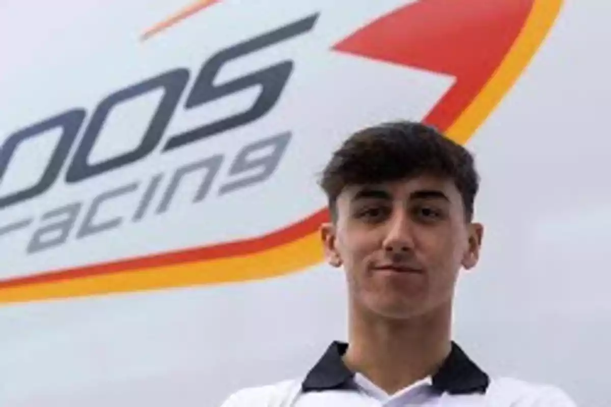 Joven con camiseta blanca posando frente a un cartel de equipo de carreras Joven con camiseta blanca posando frente a un cartel de equipo de carreras