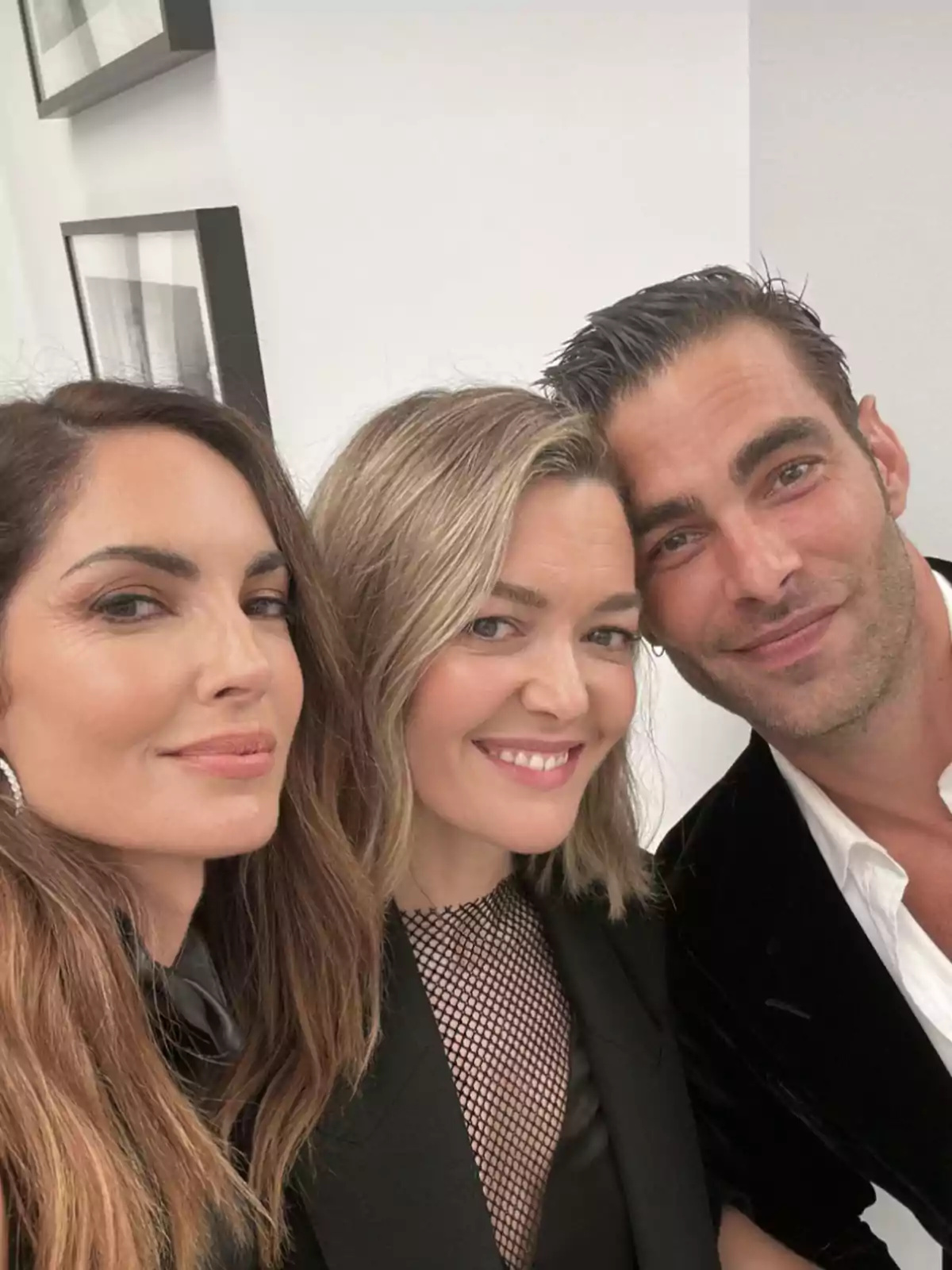 Tres personas posan juntas y sonríen para una selfie en un ambiente interior con paredes blancas y cuadros en el fondo Tres personas posan juntas y sonríen para una selfie en un ambiente interior con paredes blancas y cuadros en el fondo