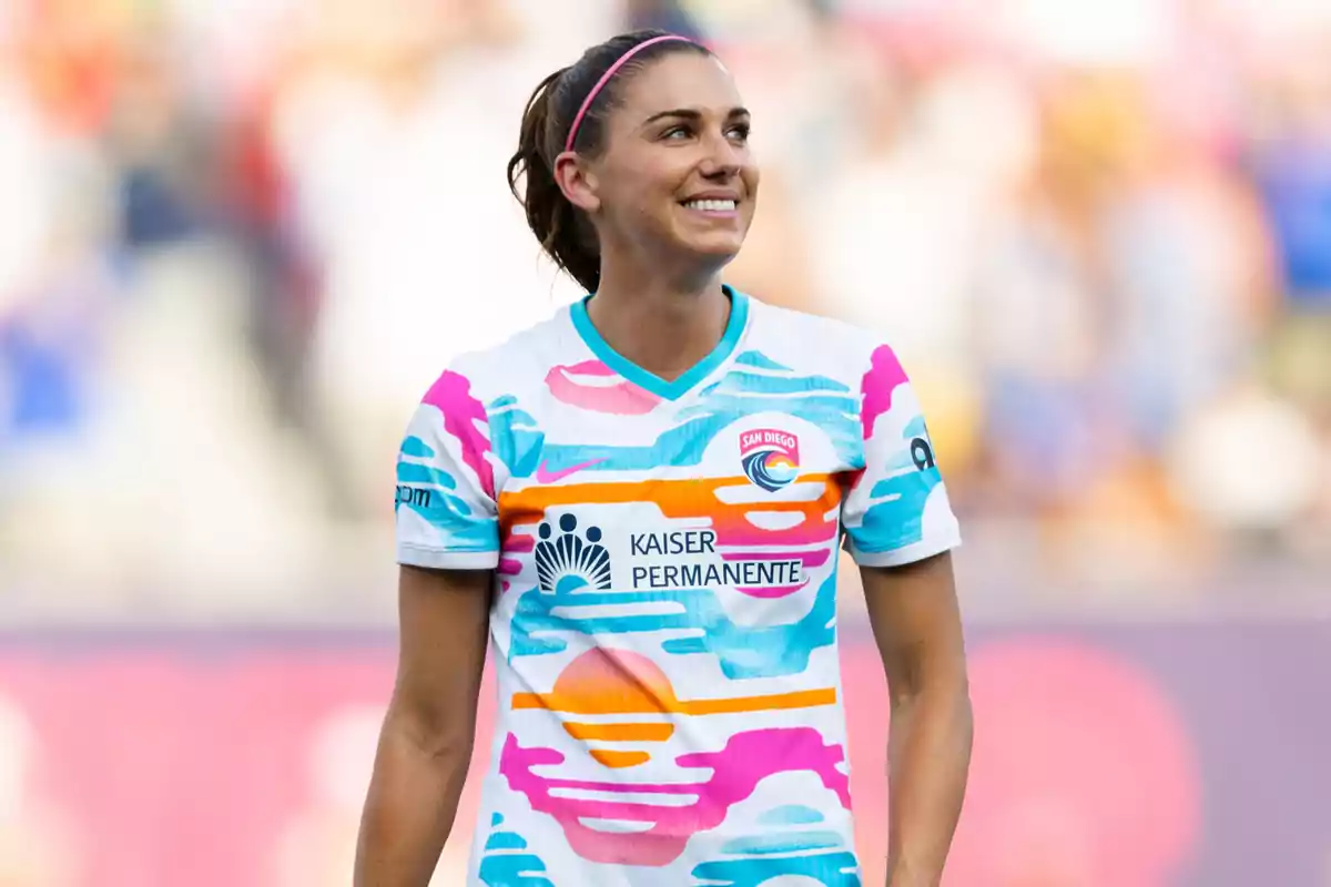 Futbolista sonriente con cinta rosa en el cabello usando un uniforme colorido del equipo San Diego en un estadio Futbolista sonriente con cinta rosa en el cabello usando un uniforme colorido del equipo San Diego en un estadio