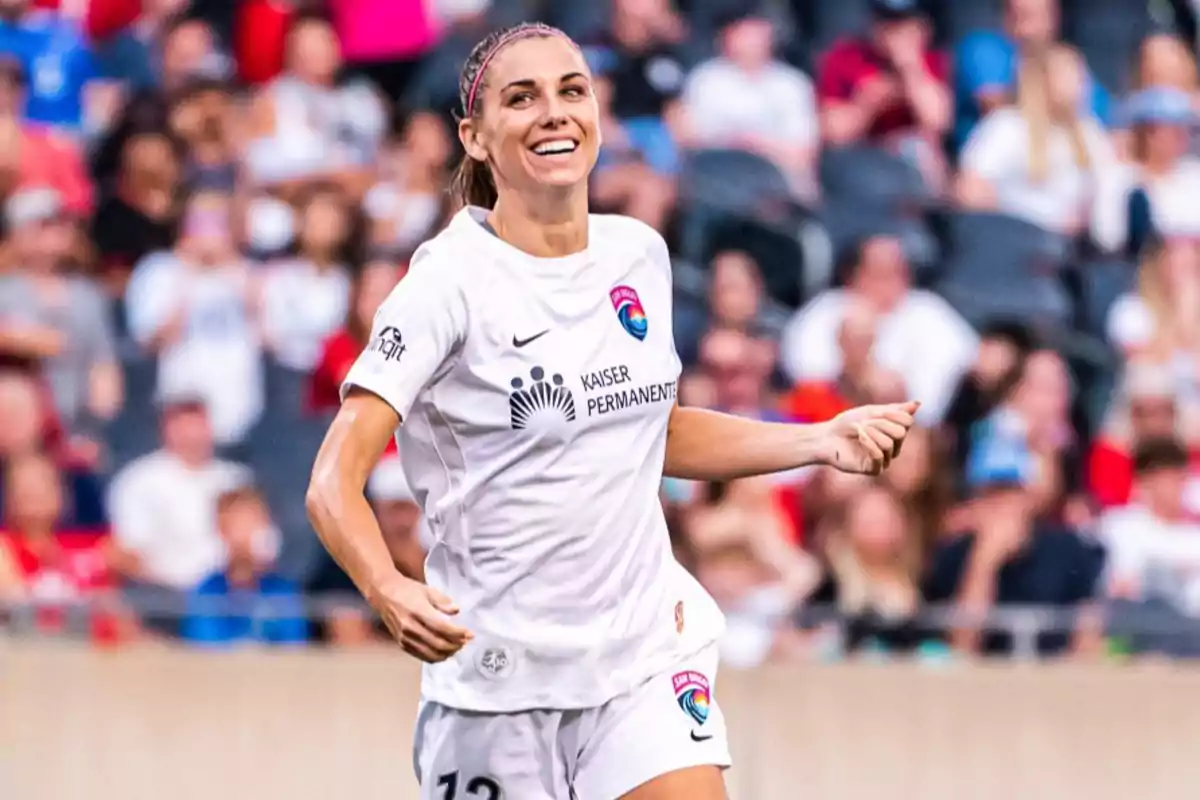 Futbolista sonriente con uniforme blanco durante un partido en un estadio lleno de espectadores Futbolista sonriente con uniforme blanco durante un partido en un estadio lleno de espectadores