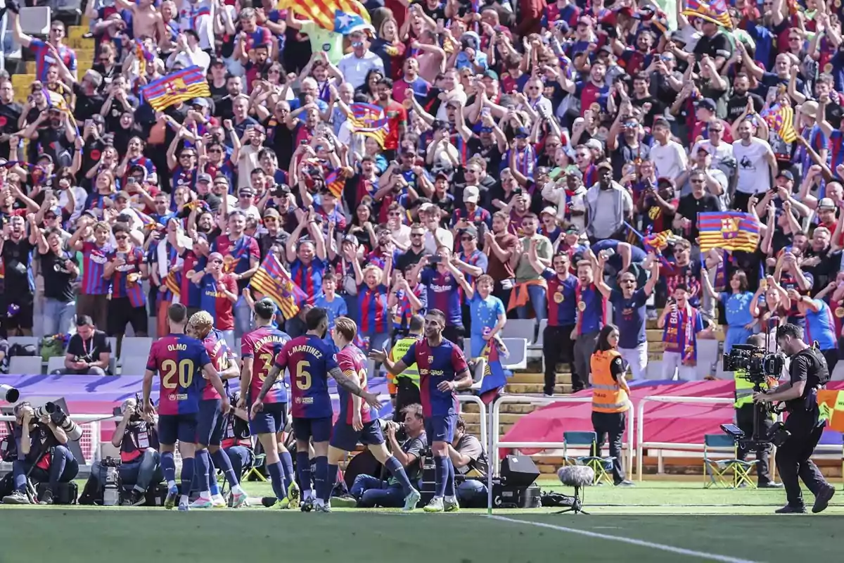 Jugadores de fútbol celebran un gol frente a una multitud de aficionados que ondean banderas y visten camisetas del equipo en las gradas del estadio