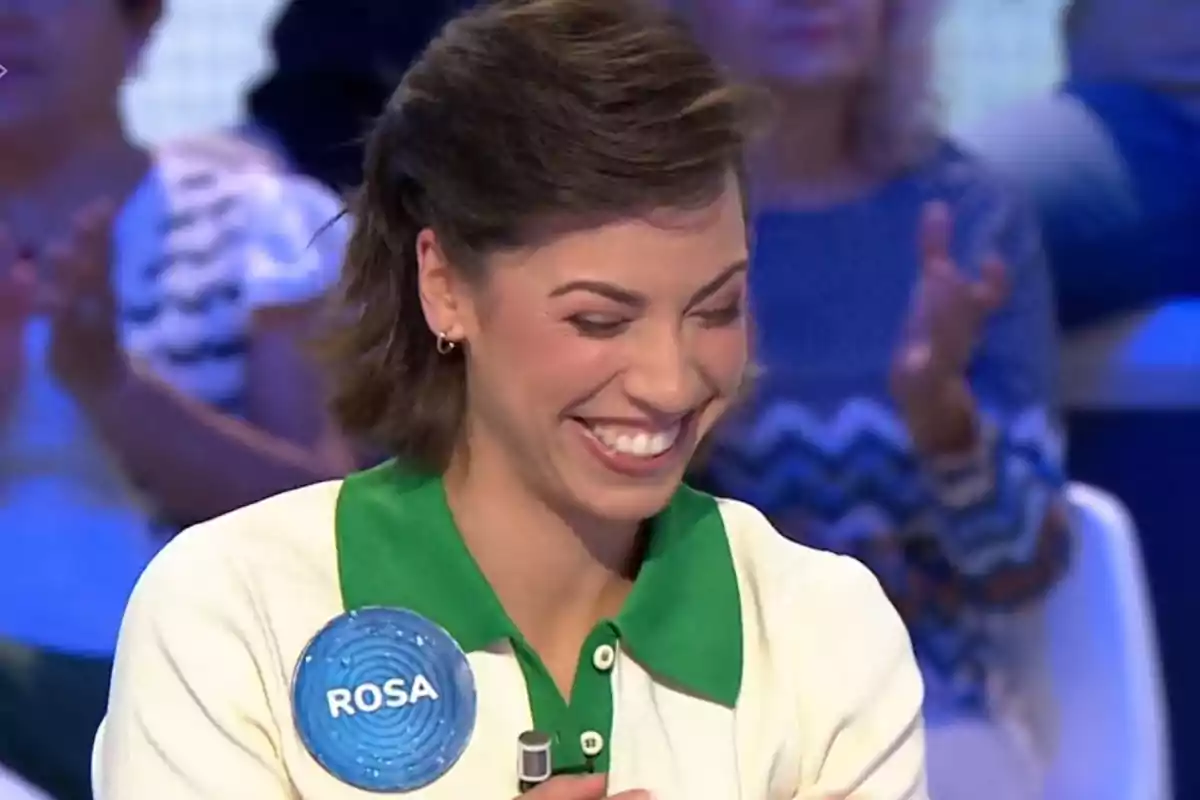 Rosa sonriente con el nombre Rosa en un pin azul durante un programa de televisión con público de fondo. Captura de 'Pasapalabra' Rosa sonriente con el nombre Rosa en un pin azul durante un programa de televisión con público de fondo. Captura de 'Pasapalabra'