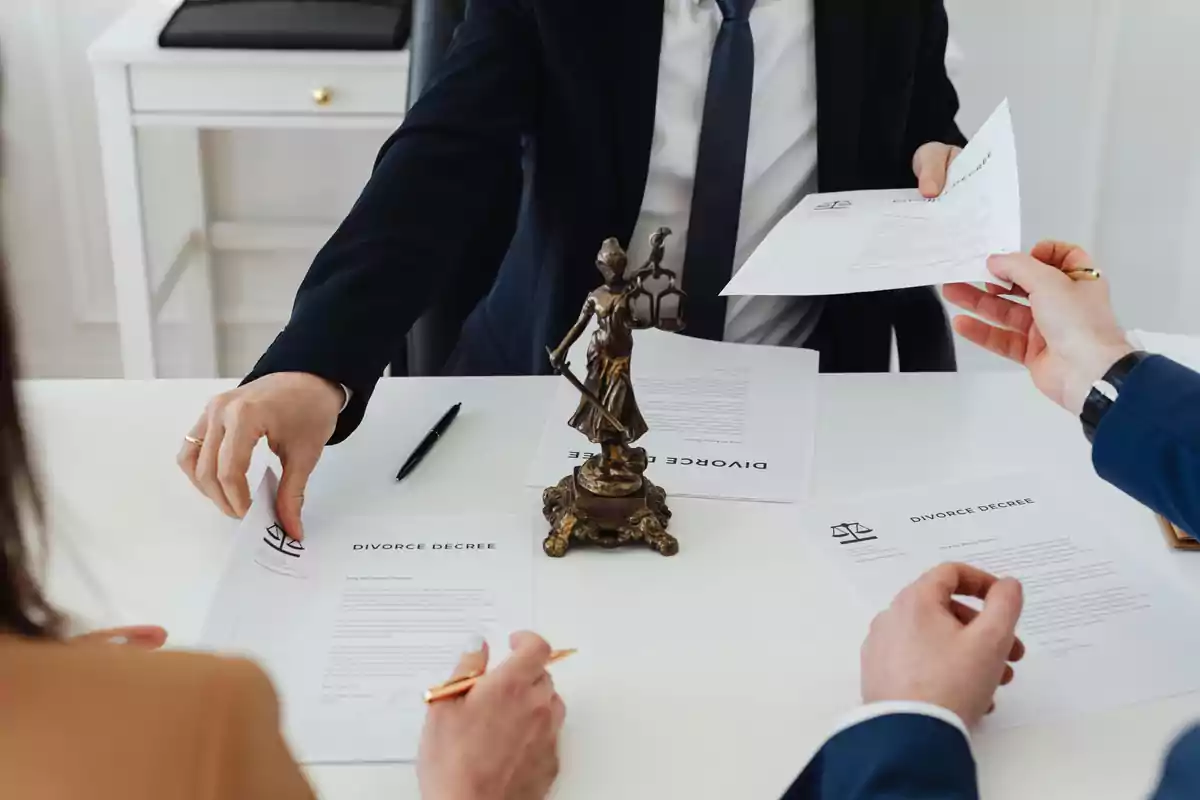 Personas en una mesa de oficina revisando y firmando documentos de divorcio con una figura de la justicia en el centro Personas en una mesa de oficina revisando y firmando documentos de divorcio con una figura de la justicia en el centro