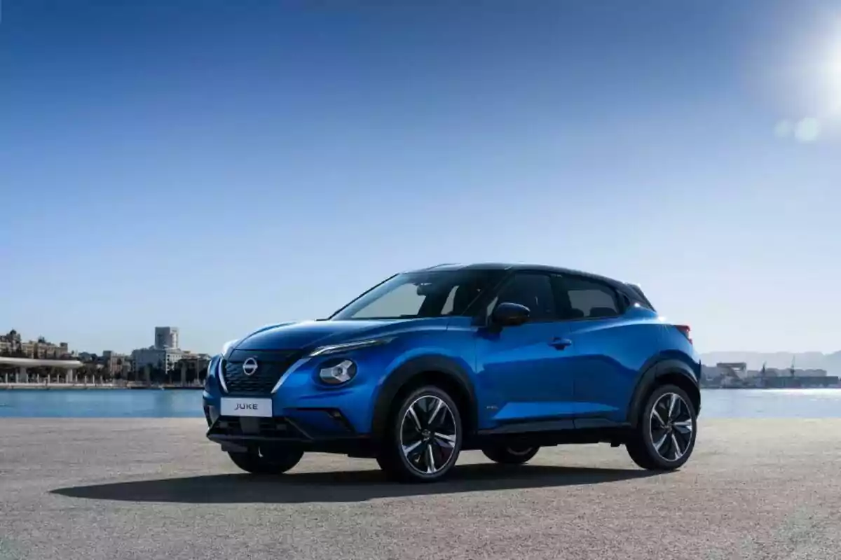 Auto Nissan Juke azul estacionado junto al mar con edificios al fondo en un día soleado Auto Nissan Juke azul estacionado junto al mar con edificios al fondo en un día soleado