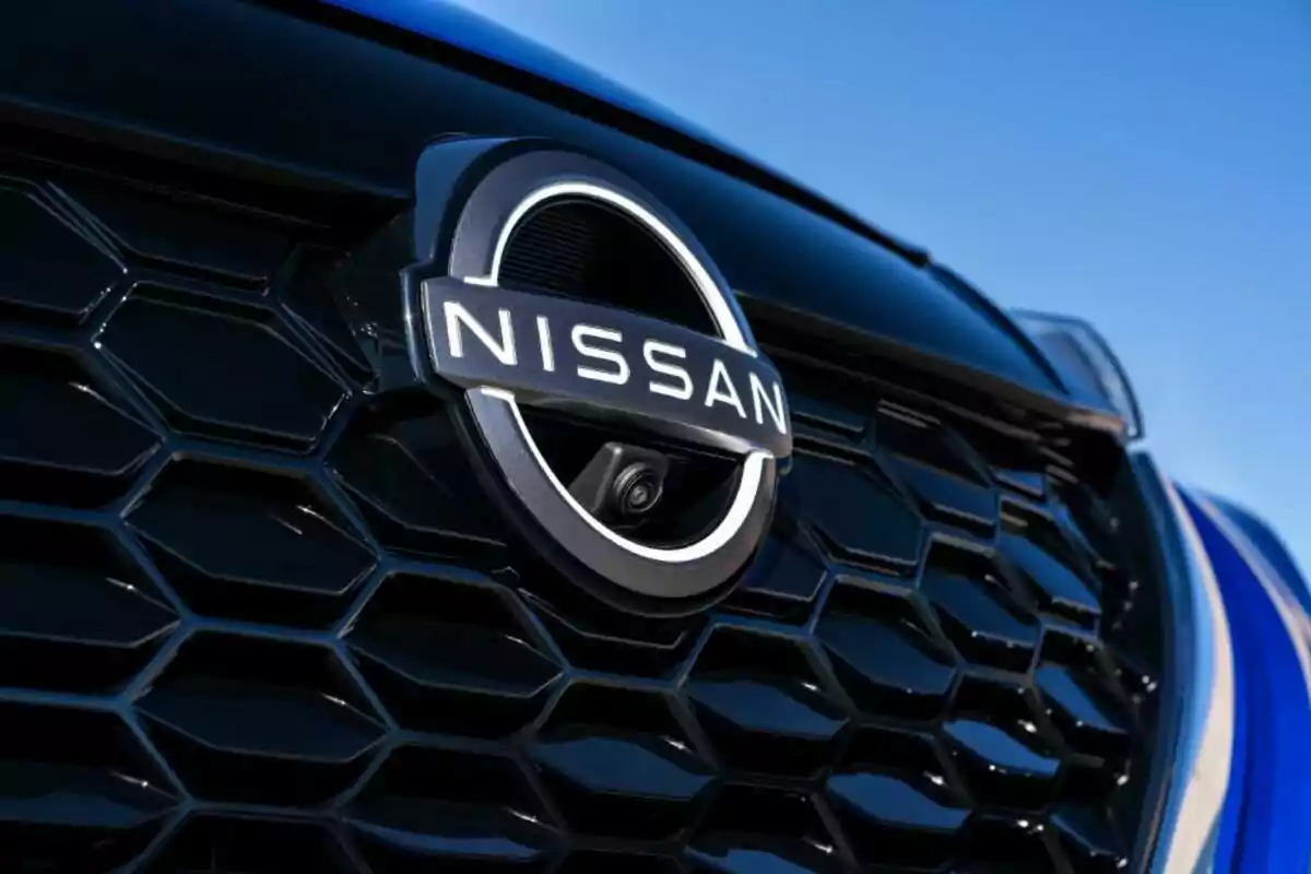 Detalle del emblema de Nissan en la parrilla frontal de un automóvil con fondo azul cielo Detalle del emblema de Nissan en la parrilla frontal de un automóvil con fondo azul cielo