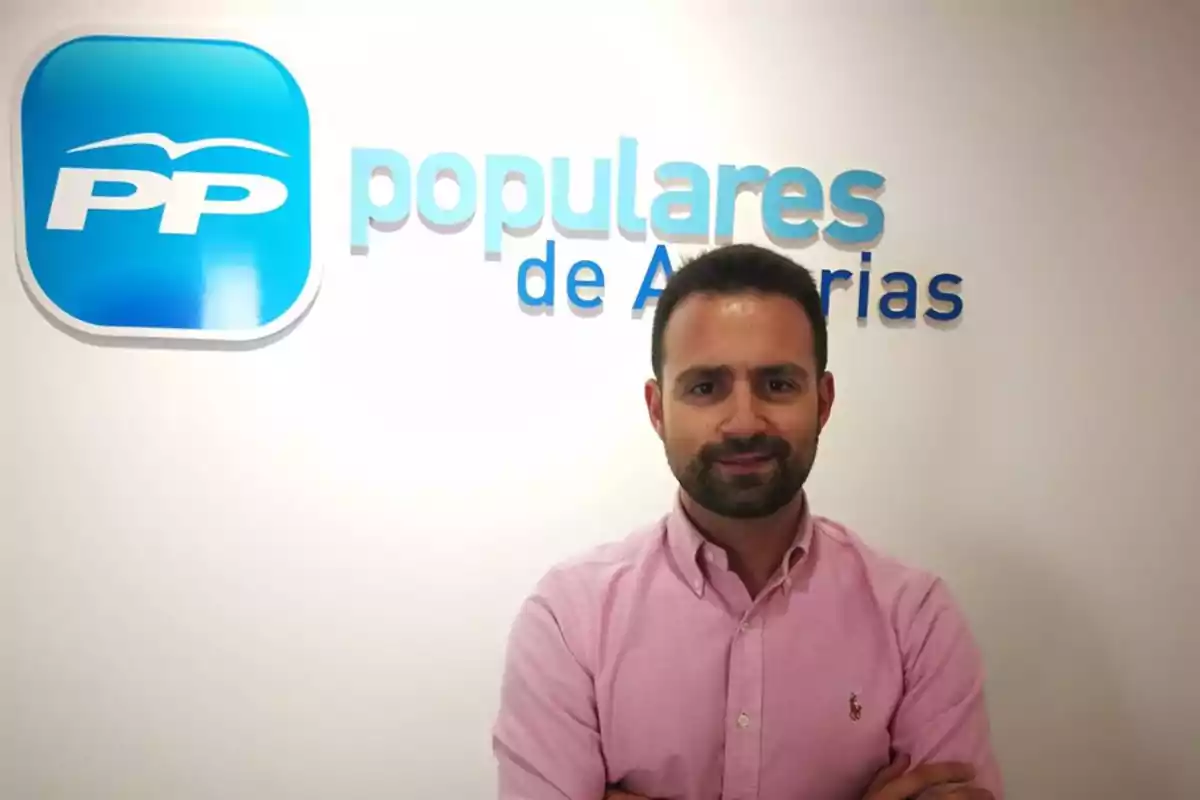 Hombre con barba y camisa rosa posando frente a una pared con el logo y nombre del Partido Popular de Asturias Hombre con barba y camisa rosa posando frente a una pared con el logo y nombre del Partido Popular de Asturias