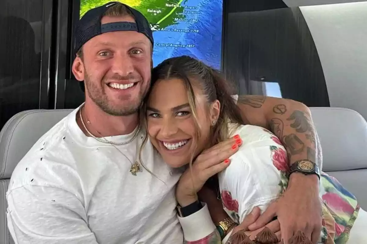 Pareja sonriente abrazándose dentro de un avión privado con un mapa en la pantalla de fondo Pareja sonriente abrazándose dentro de un avión privado con un mapa en la pantalla de fondo