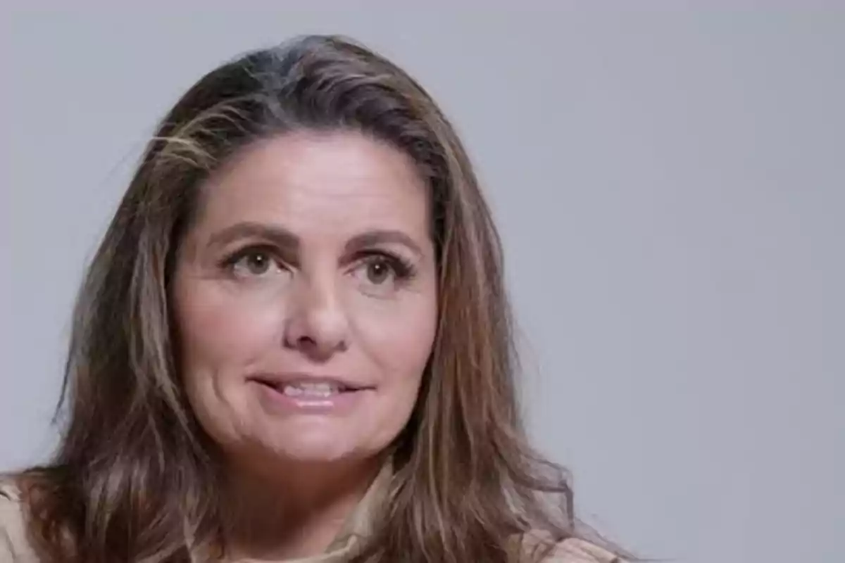 Mujer de cabello castaño largo con expresión facial neutral y fondo gris claro Mujer de cabello castaño largo con expresión facial neutral y fondo gris claro