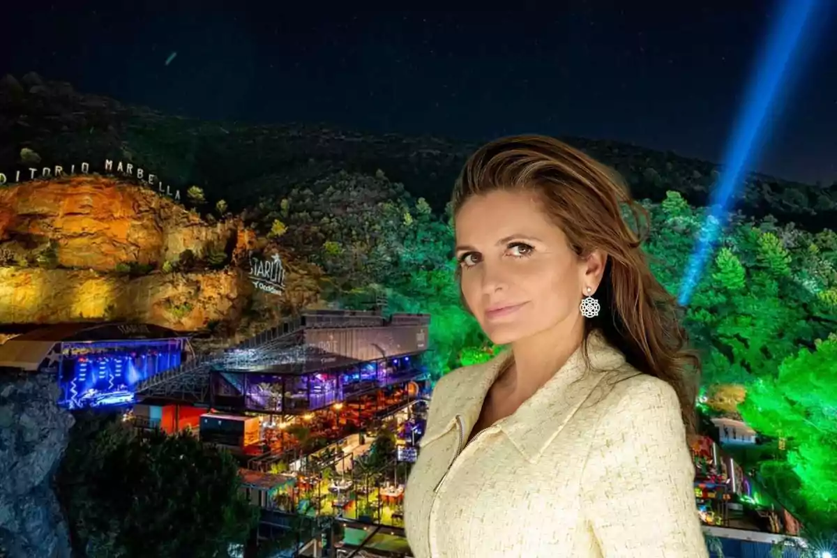 Mujer de cabello castaño claro y chaqueta beige posando frente a un auditorio iluminado en la noche rodeado de vegetación y luces de colores