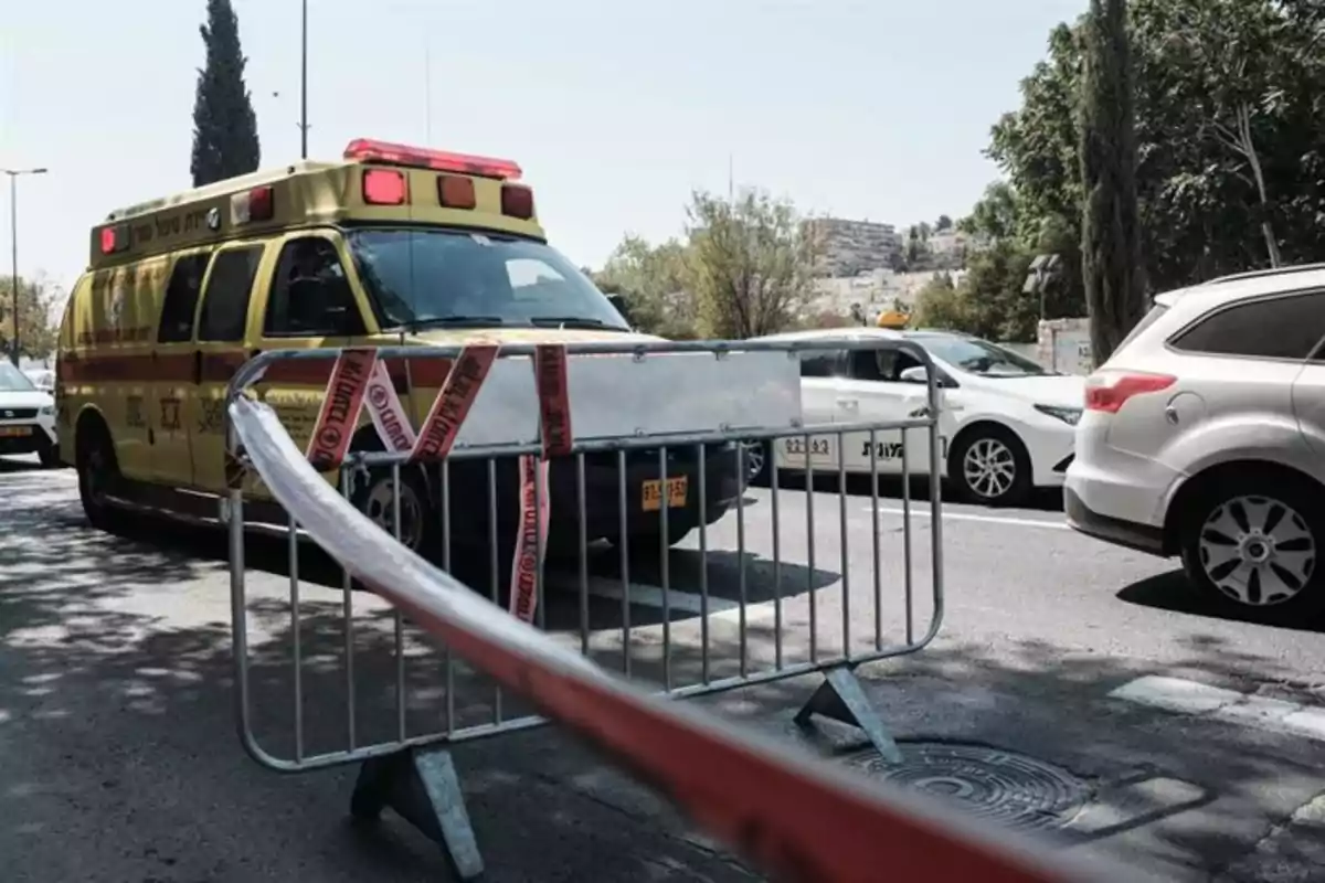 Ambulancia amarilla detrás de una valla de seguridad con cinta de advertencia en una calle junto a varios autos blancos Ambulancia amarilla detrás de una valla de seguridad con cinta de advertencia en una calle junto a varios autos blancos