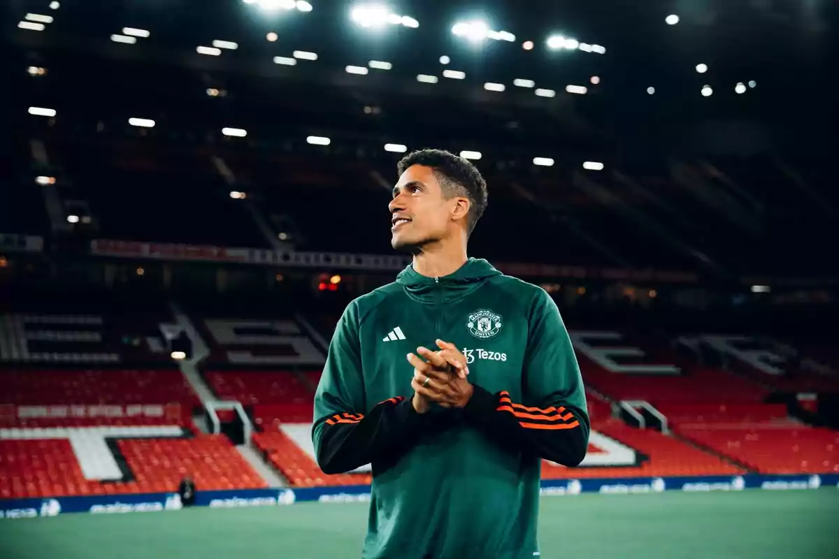 Futbolista con sudadera verde del Manchester United de pie en un estadio iluminado Futbolista con sudadera verde del Manchester United de pie en un estadio iluminado