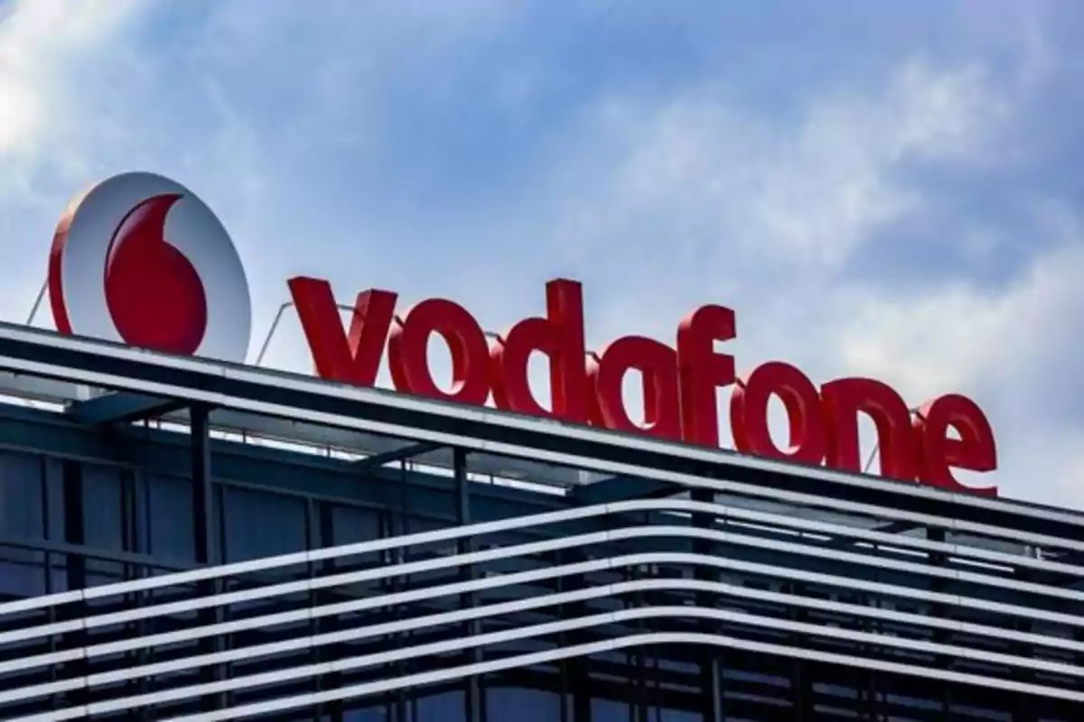 Edificio moderno con el logo de Vodafone en la parte superior bajo un cielo parcialmente nublado Edificio moderno con el logo de Vodafone en la parte superior bajo un cielo parcialmente nublado