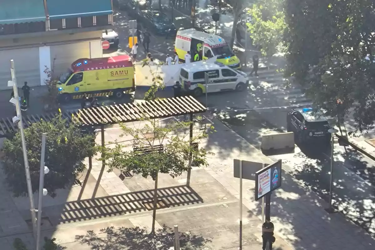 Vista aérea de una calle acordonada con presencia de ambulancias, un vehículo policial y personal de emergencia atendiendo una situación