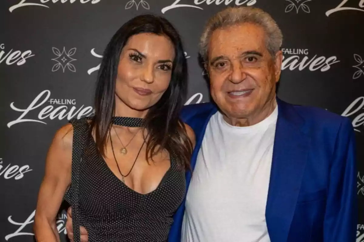 Una mujer y un hombre posan juntos sonriendo frente a un fondo negro con el texto Falling Leaves repetido Una mujer y un hombre posan juntos sonriendo frente a un fondo negro con el texto Falling Leaves repetido