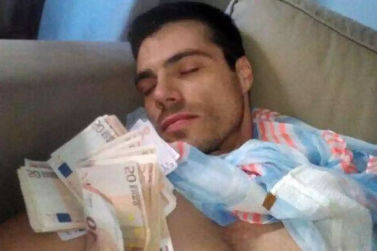 Hombre durmiendo en un sofá con billetes de euro en la mano y una bufanda alrededor del cuello.