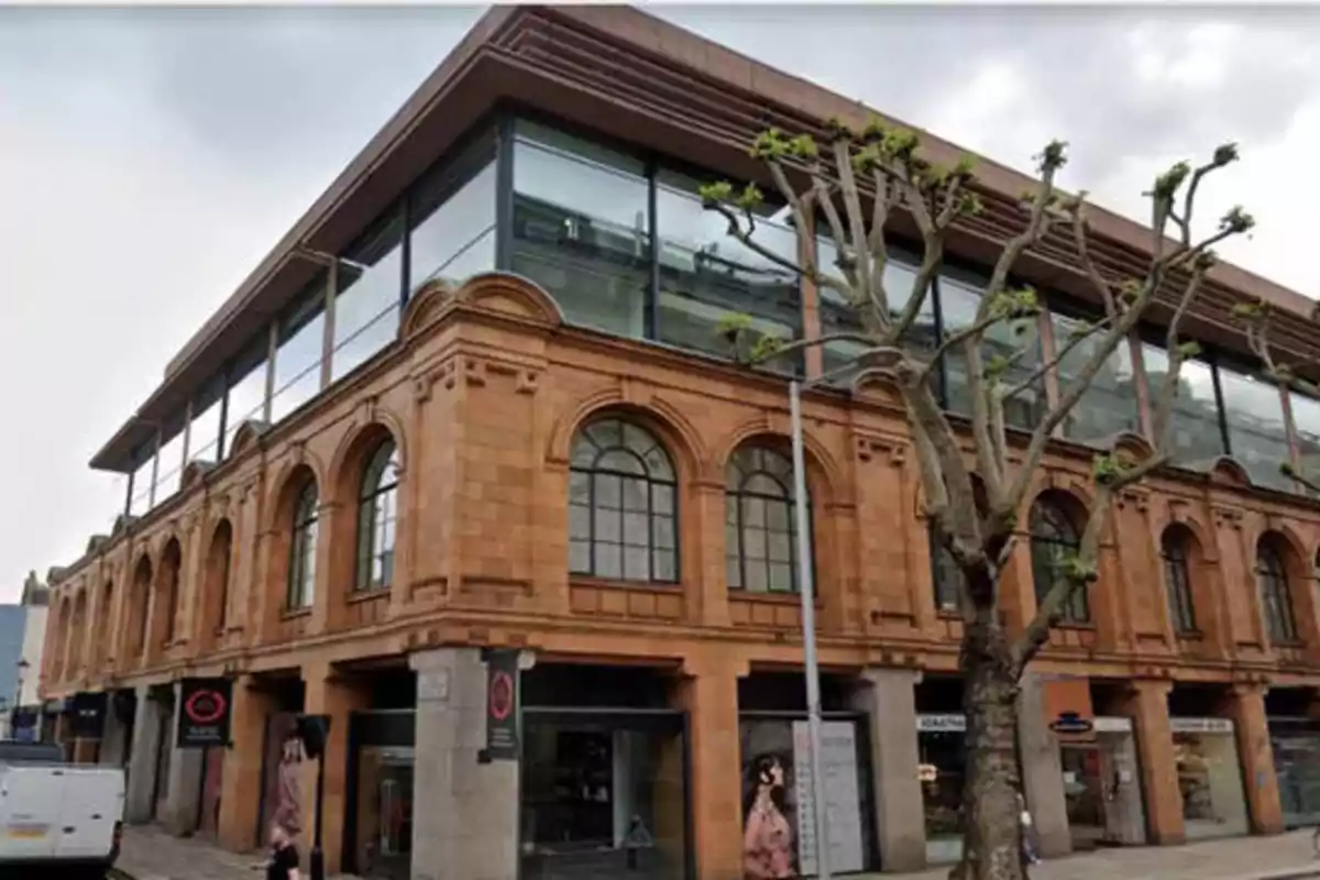 Edificio de ladrillo con ventanas arqueadas y un árbol sin hojas en la acera.