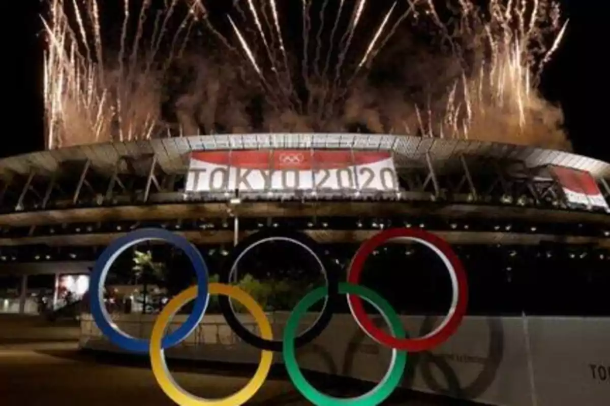 Estadio olímpico de Tokio 2020 con fuegos artificiales y los anillos olímpicos en primer plano.