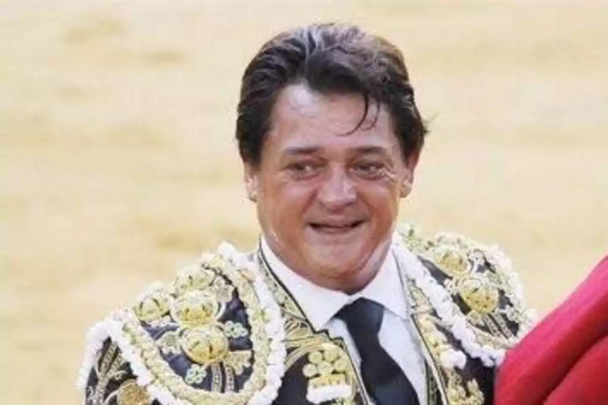 Un torero sonriente con traje de luces en una plaza de toros.