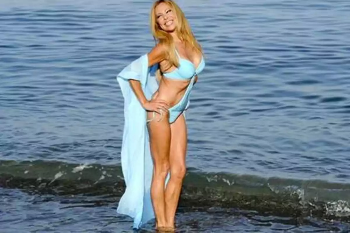 Mujer en bikini azul posando en la orilla del mar.